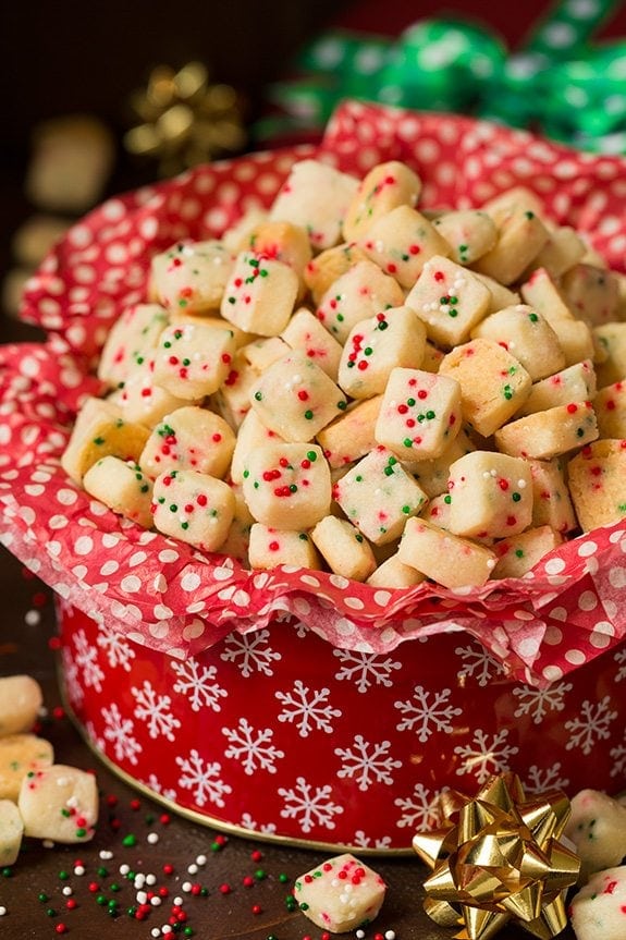 A red Christmas tin full of red tissue paper and funfetti shortbread bites, full of red and green sprinkles.