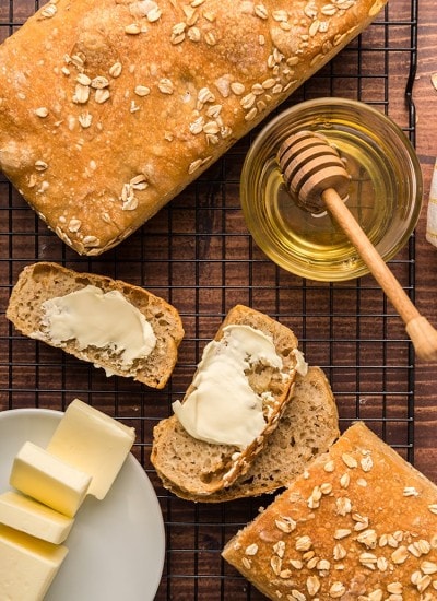 Above shot of oat bread sliced with butter and honey on a cooling rack.