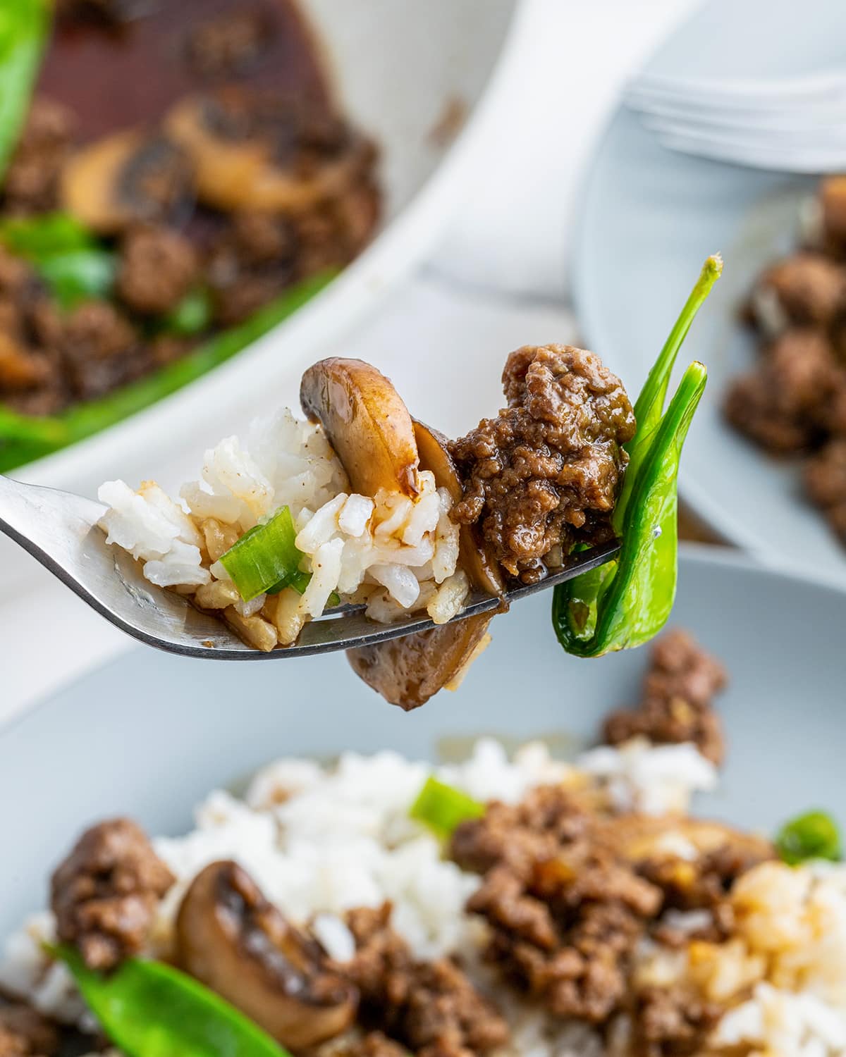 A bite of rice, asian beef and snow peas on a fork.