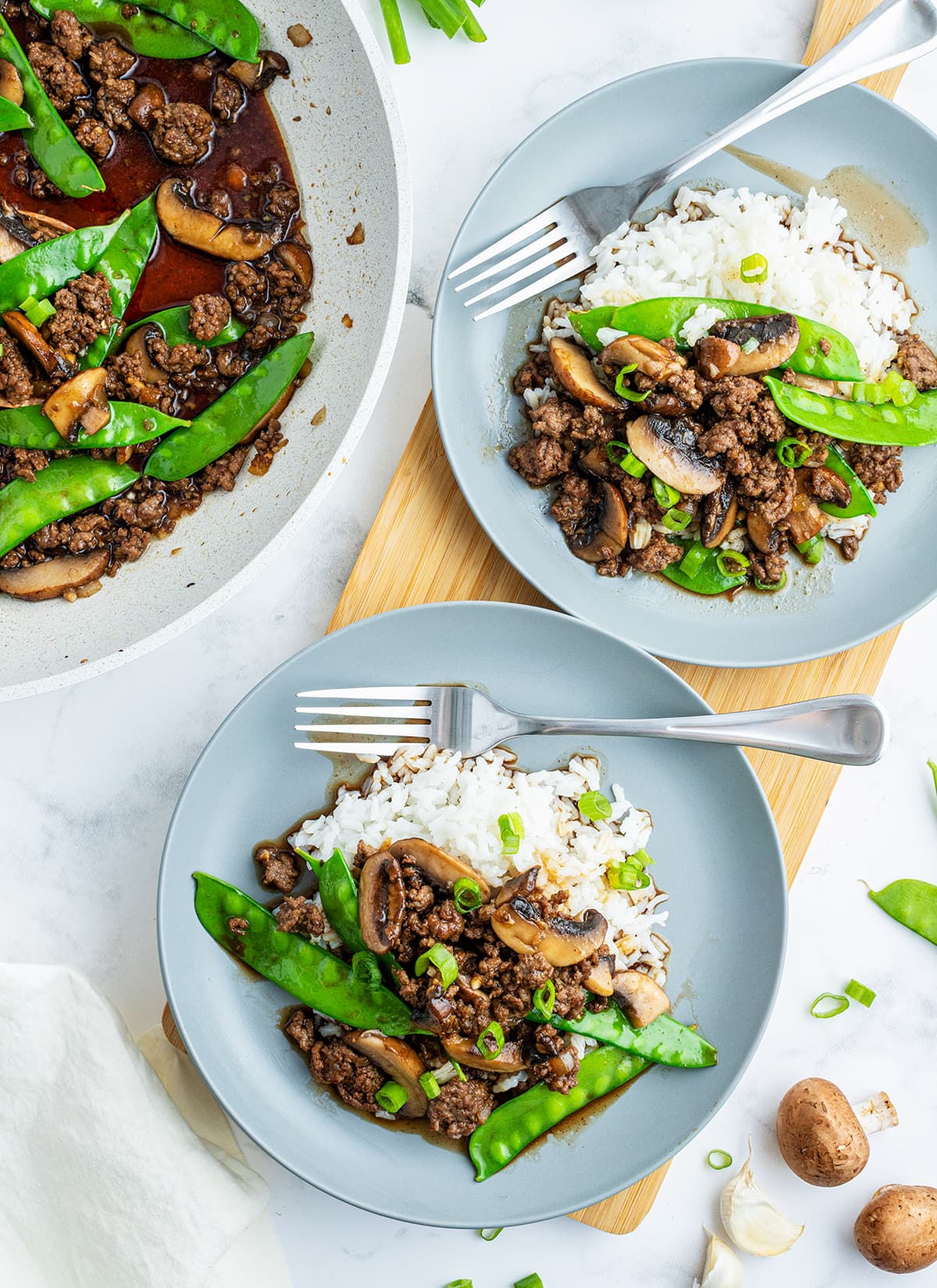 An overhead photo of two plates of asian beef with snow peas on top of white rice.