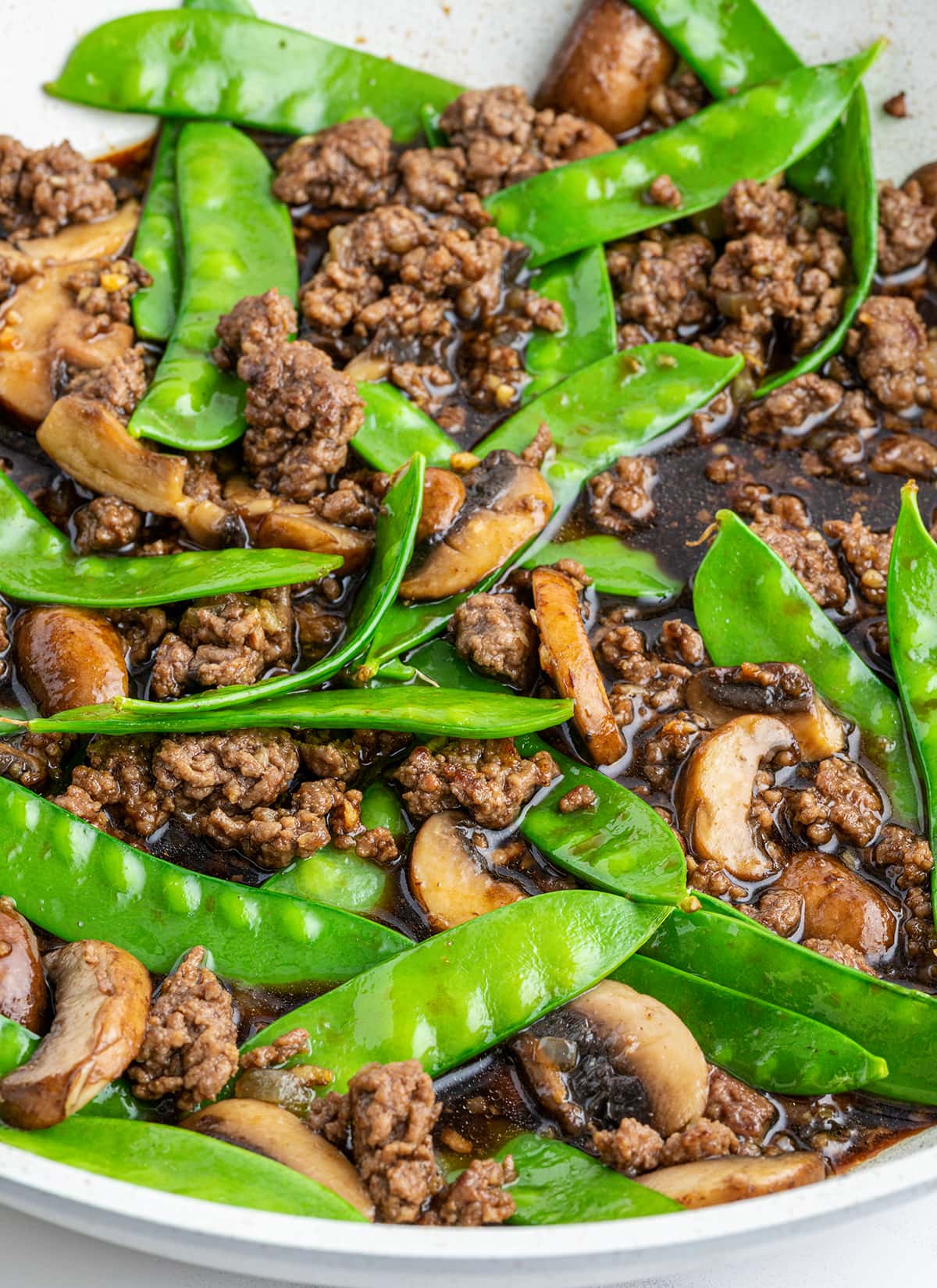 A pan of Asian Beef with snow peas and mushrooms in a teriyaki sauce.