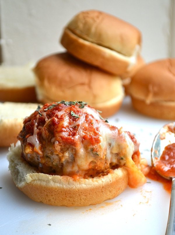 Angled view of cheesy stuffed meatball sliders on a white plate.