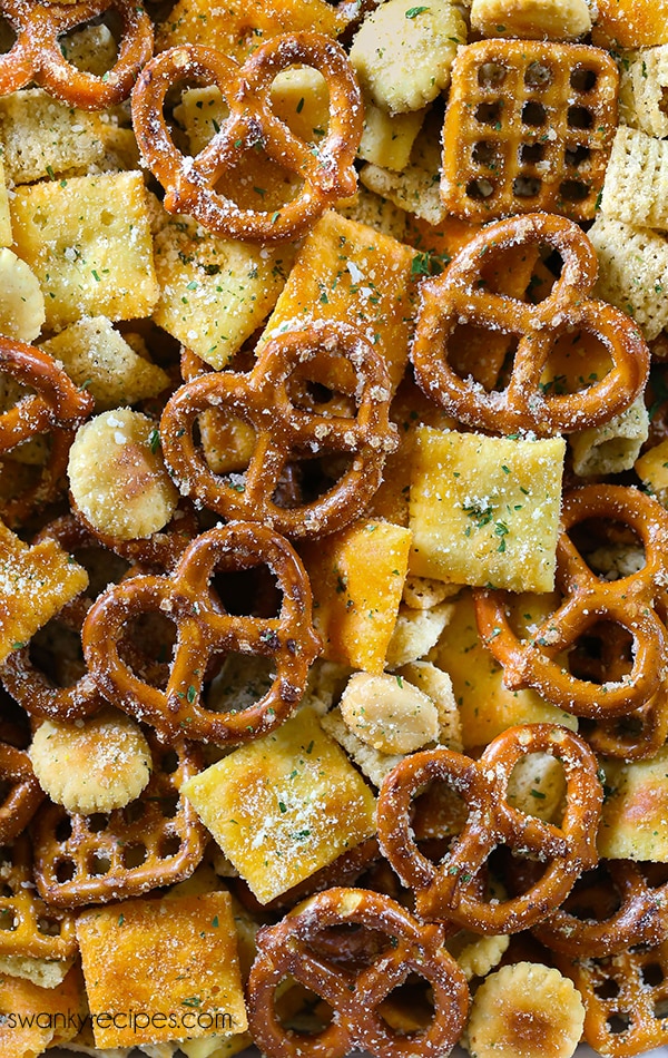 A close up of a snack chex mix coated in ranch seasoning. There are pretzels and small crackers.