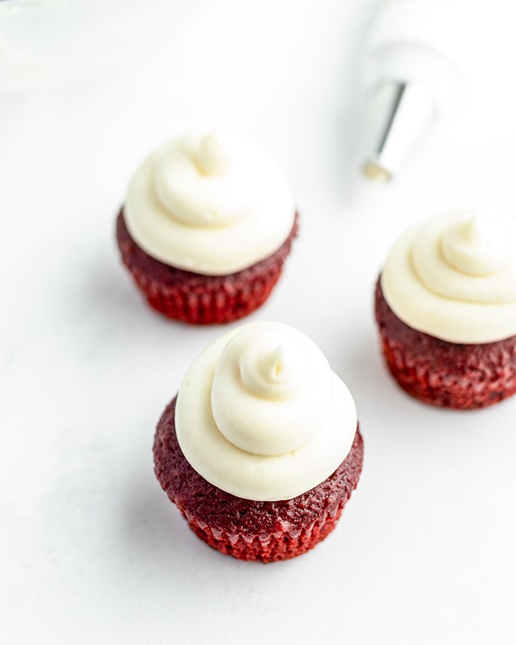 Cream cheese frosting piped on top of red velvet cupcakes