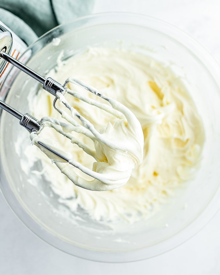 Cream Cheese frosting on hand mixer beaters, above a bowl of it. 