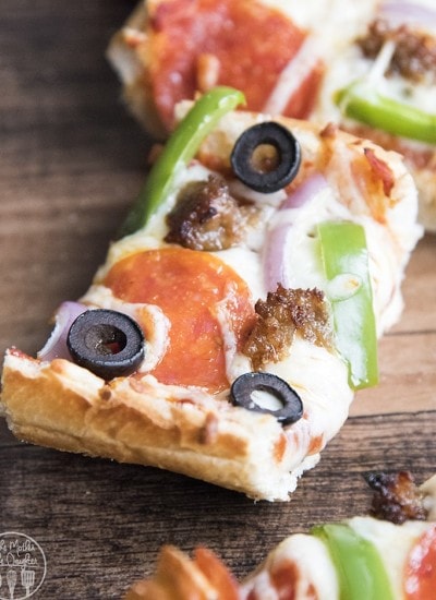 A piece of pizza made with french bread for the crust. The pizza is topped with pepperoni, sausage, green pepper, red onion, and olive.