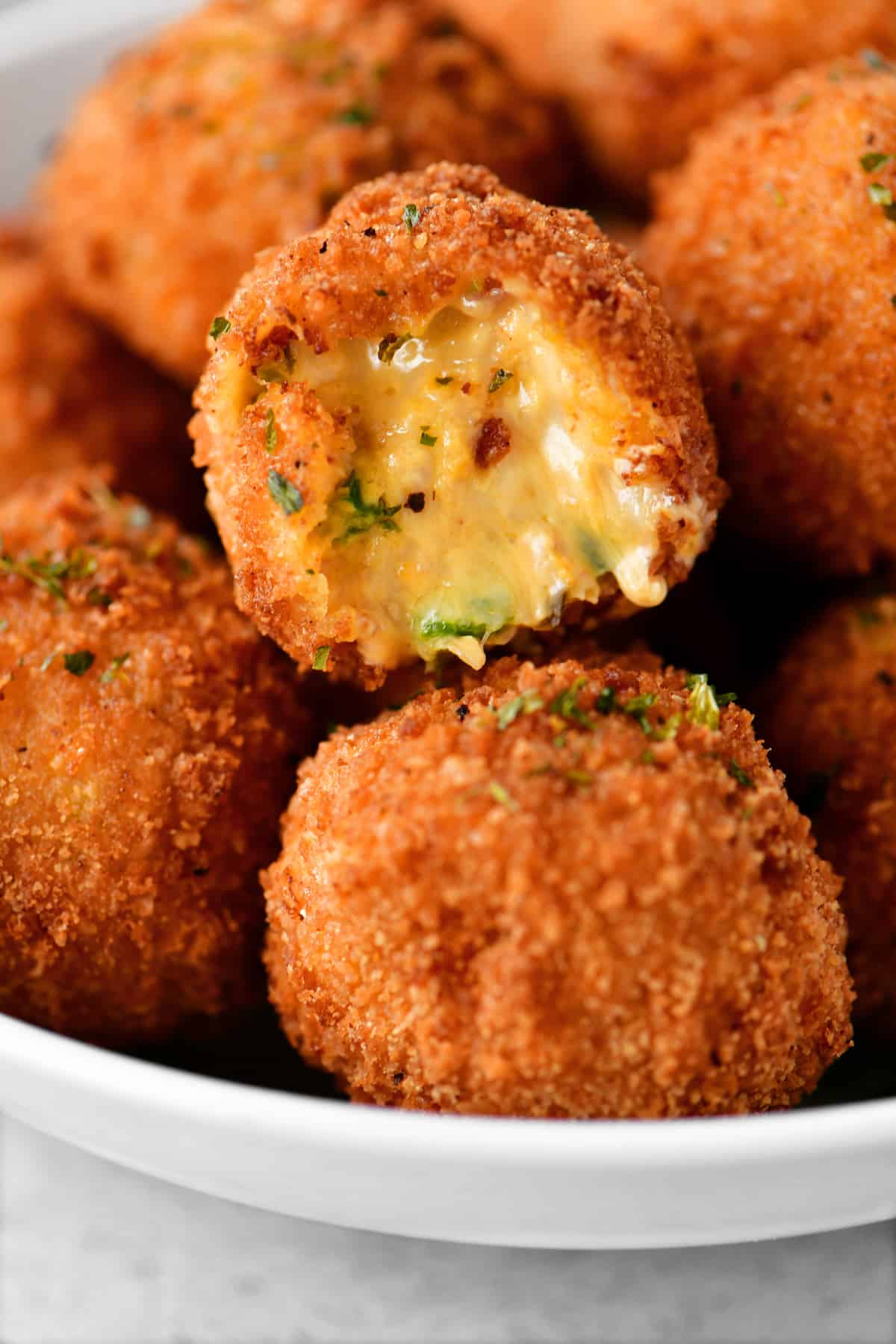 A bowl of cheesy bites covered in breading, they look deep fried, and there are pieces of jalapenos and bacon in them.