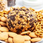 A peanut butter cheese ball wrapped in chocolate chips and peanut butter chips on a plate with pretzels and cookies.