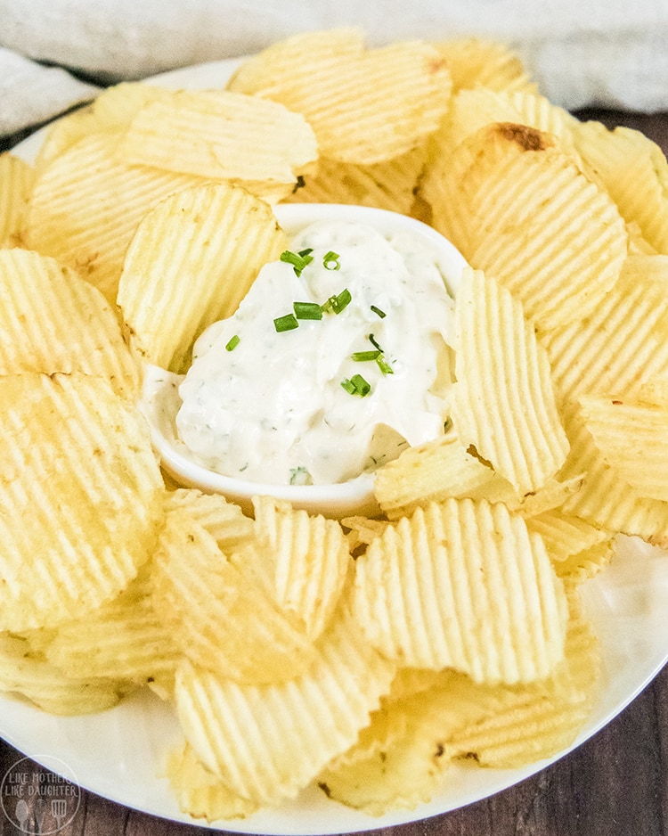 Close up shot of potato chips surrounding a white bowl with ranch dip inside of it.