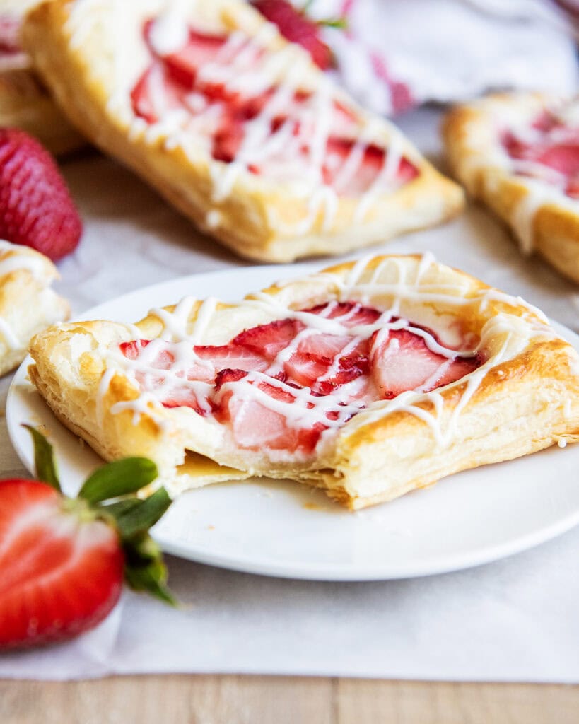 A cream cheese and strawberry danish on a plate with a bite out of it.