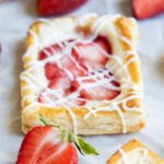 A Strawberry Danish drizzled with vanilla icing and surrounded by fresh strawberries.