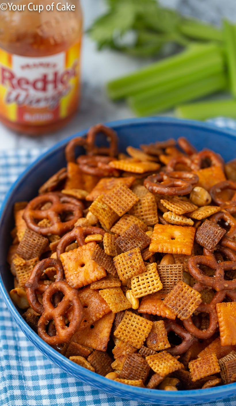 A bowl of buffalo chex mix, it is darker in color with cheese nips, pretzels, and mixed nuts.