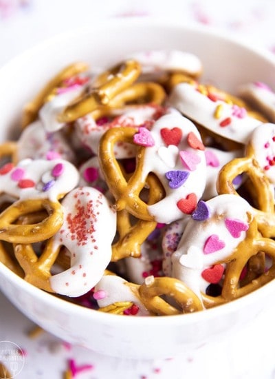 Close up image of valentine's day pretzels dipped in white chocolate and topped with sprinkles in a bowl.