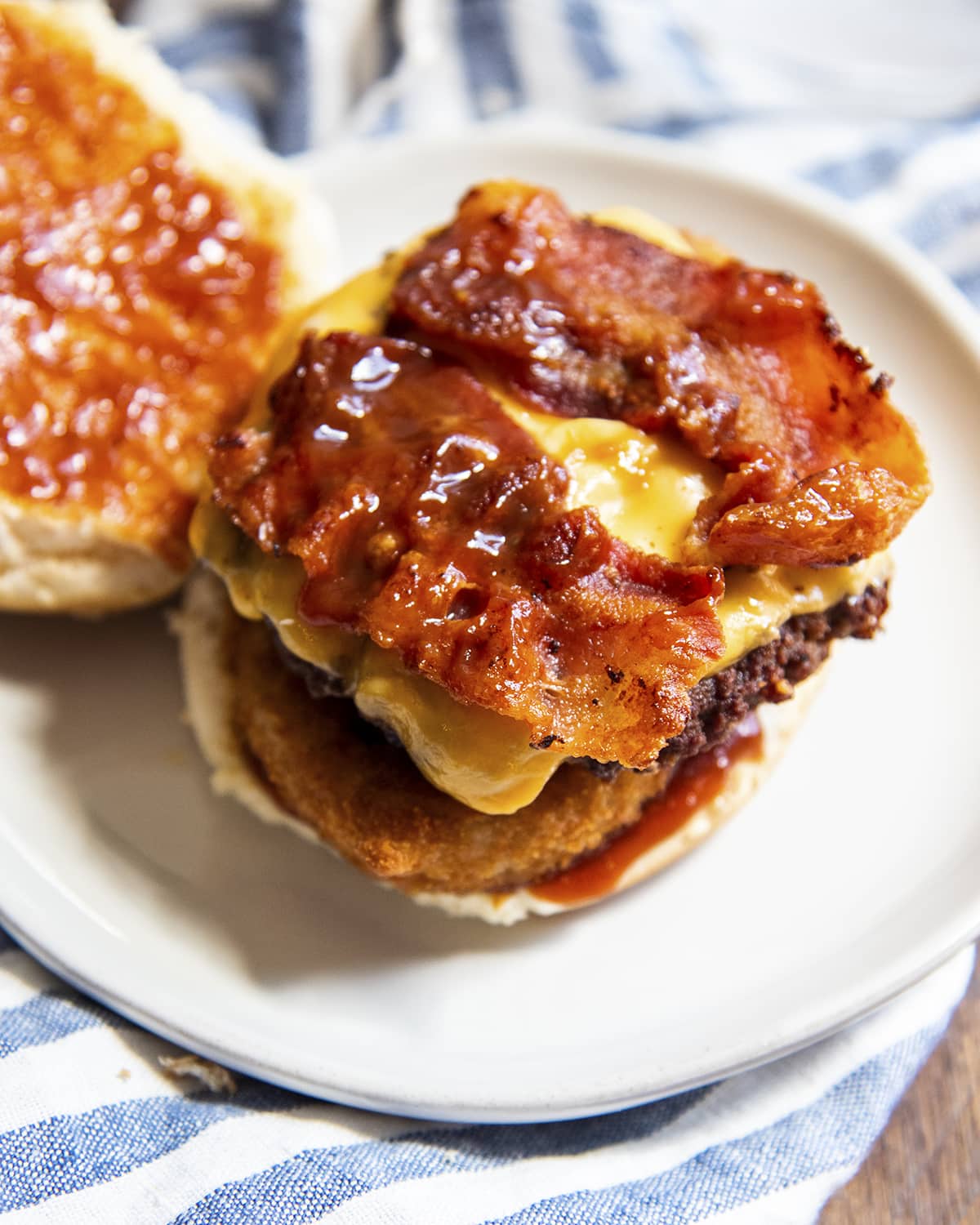 A cheeseburger with the top bun off topped with bacon and barbecue sauce.
