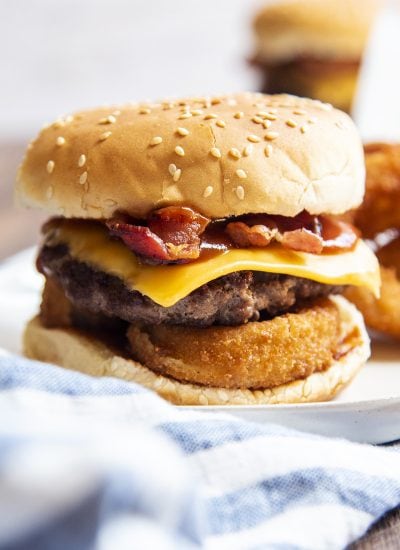 A cheeseburger with onion rings, bacon, and bbq sauce in a bun on a plate.