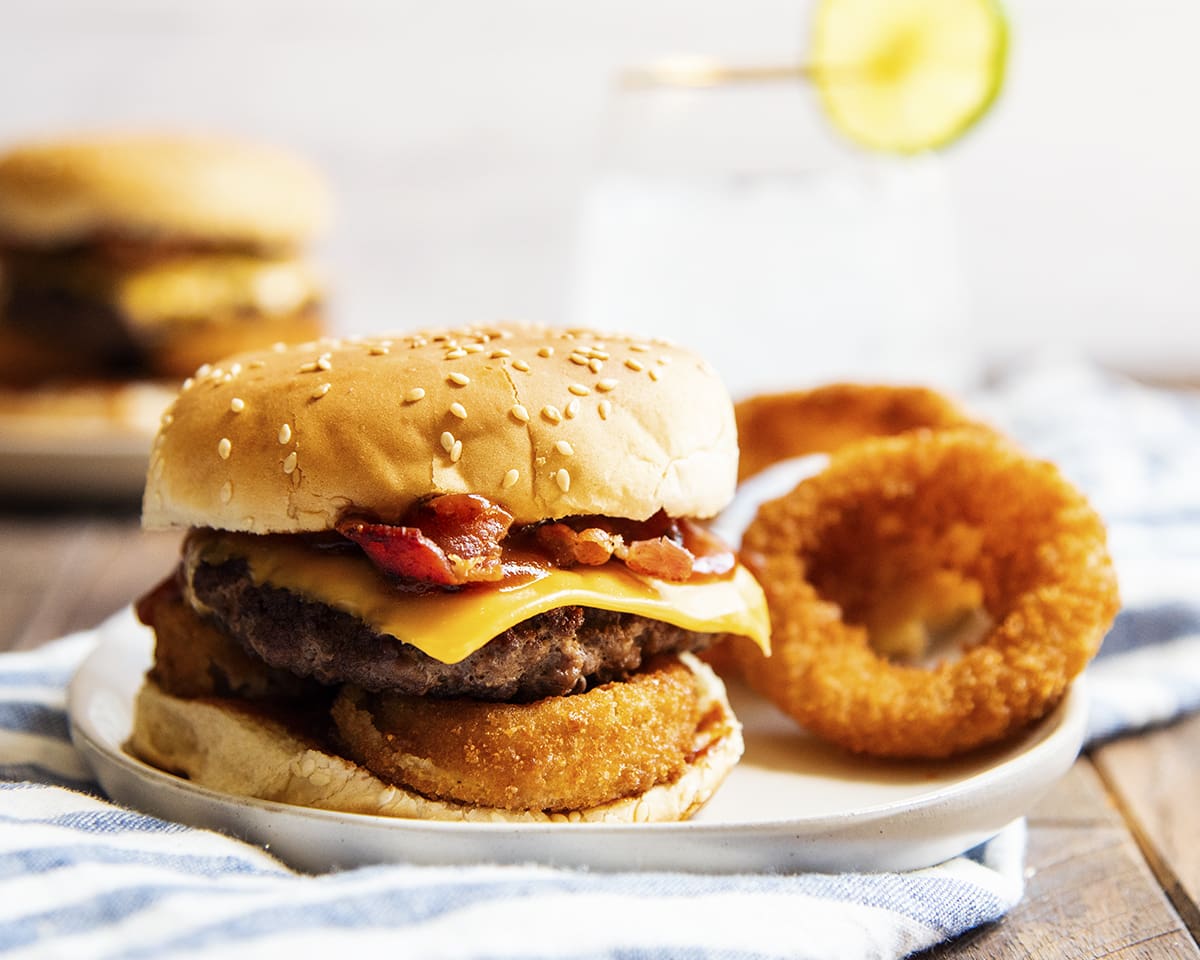 A western bacon cheeseburger on a plate with onion rings.