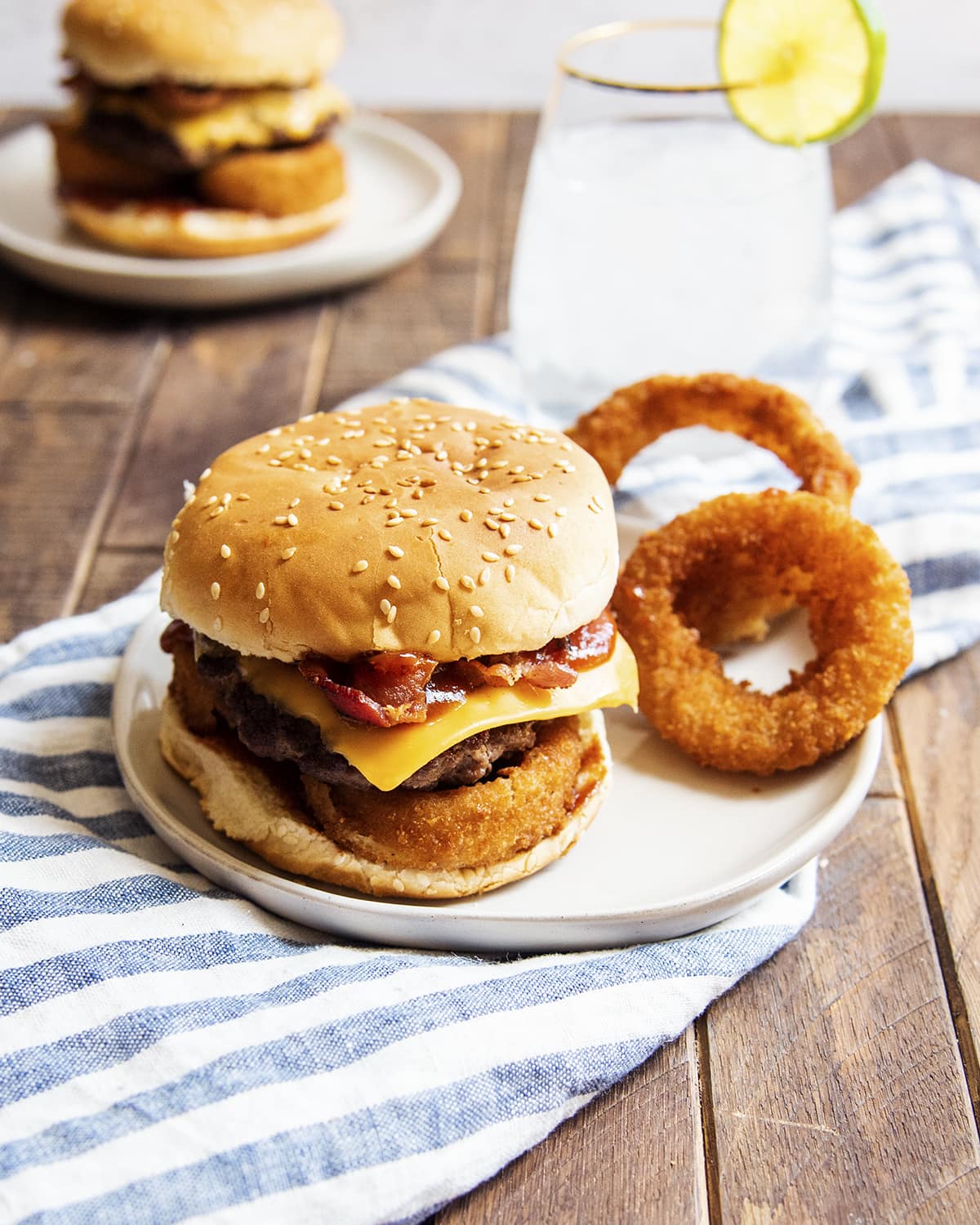 A bacon cheeseburger with onion rings on a white plate.