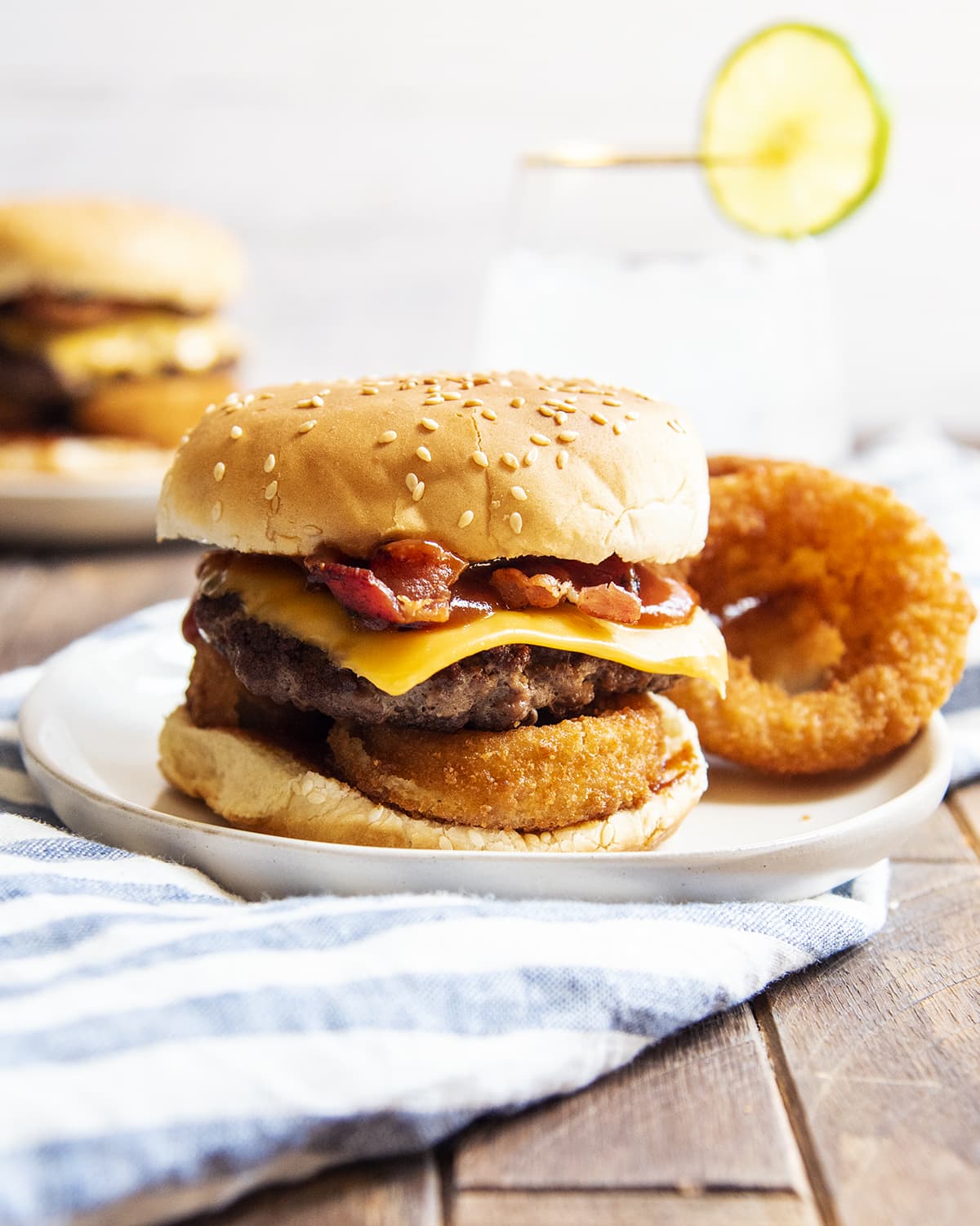 A western bacon cheeseburger with an onion ring under the burger patty on a plate.