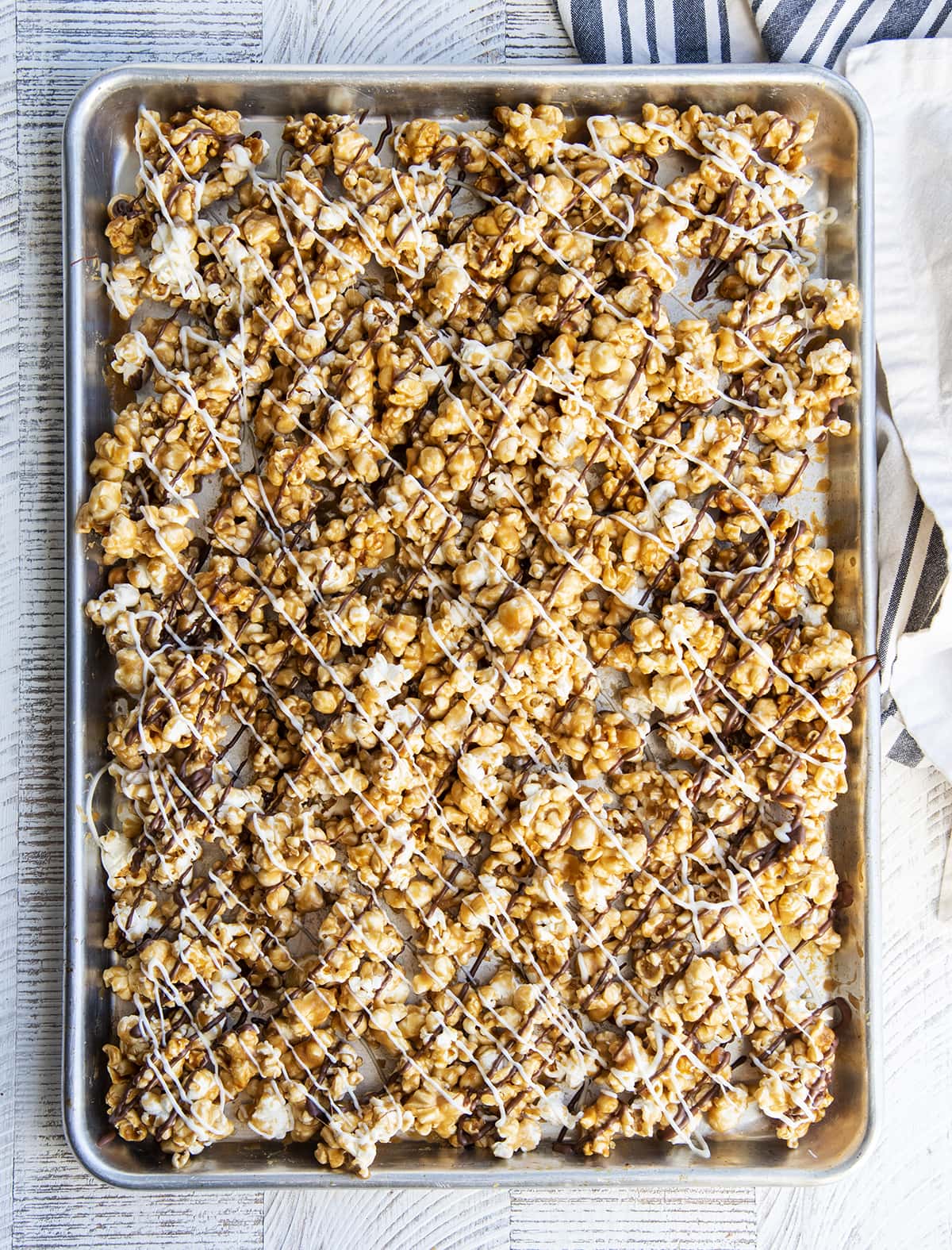 An overhead photo of a baking pan topped with caramel popcorn drizzled with chocolate and white chocolate. 