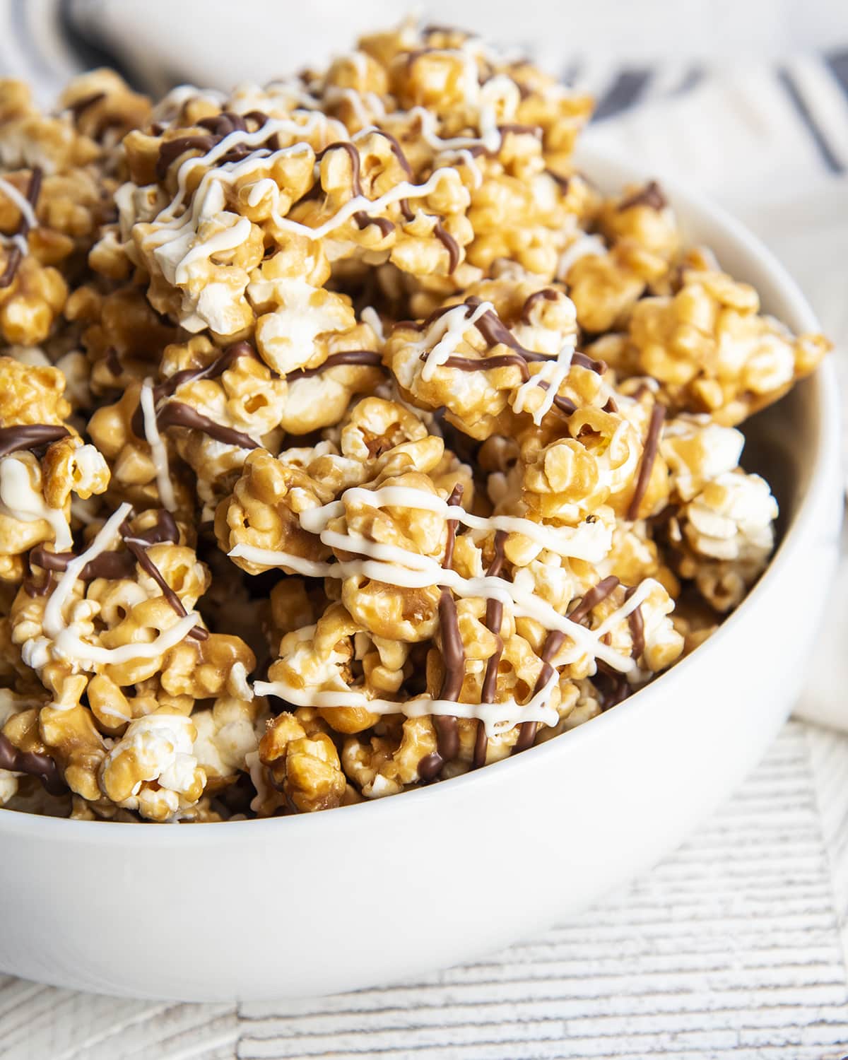 A bowl of zebra popcorn with a golden caramel color, and drizzled with chocolate, and white chocolate.