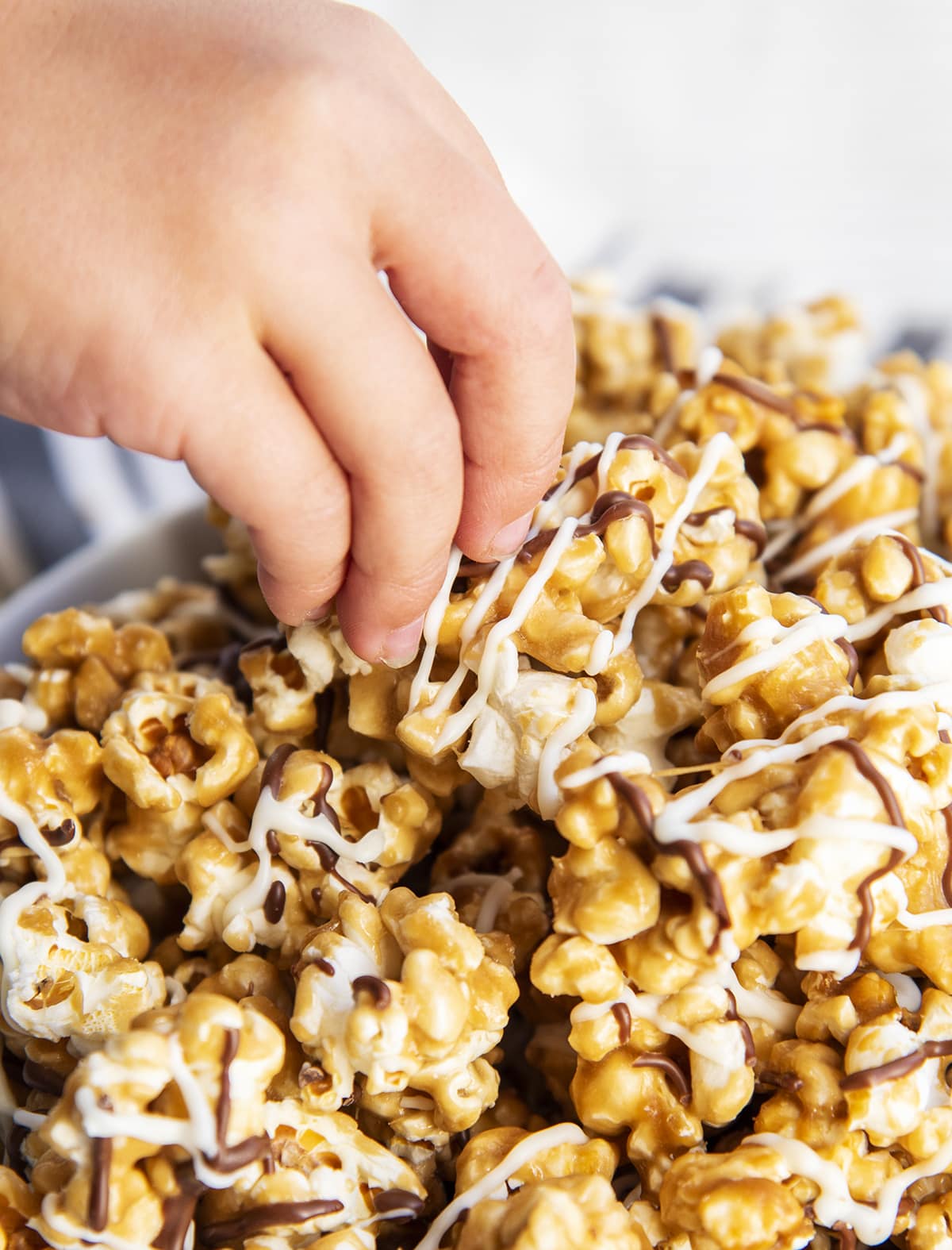 A hand grabbing a piece of caramel popcorn out of a bowl.