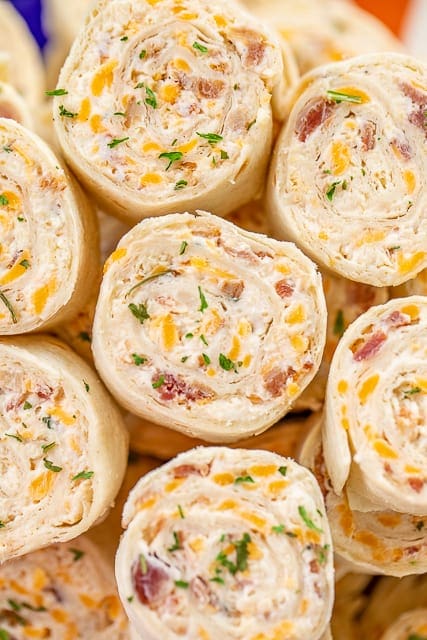 Pinwheels made with tortillas rolled up with cream cheese, bacon, cheddar cheese, and sprinkled with parsley.