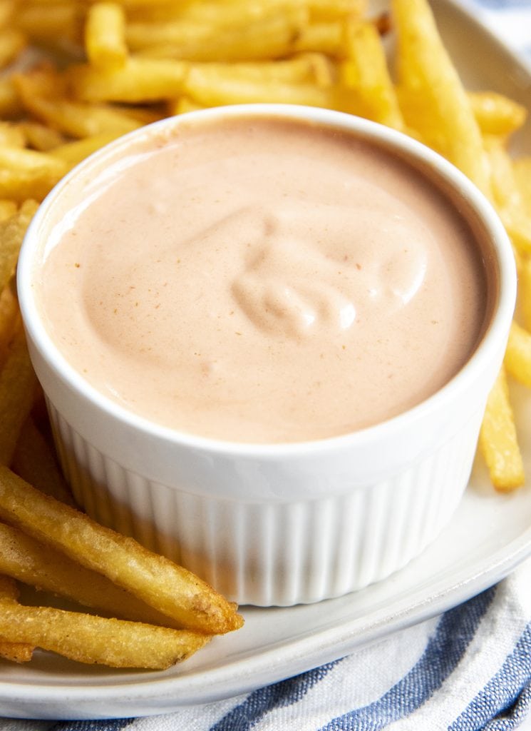 A bowl of french fry sauce on a plate with french fries.
