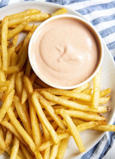 An overhead photo of a small bowl of french fry sauce on a plate of french fries.