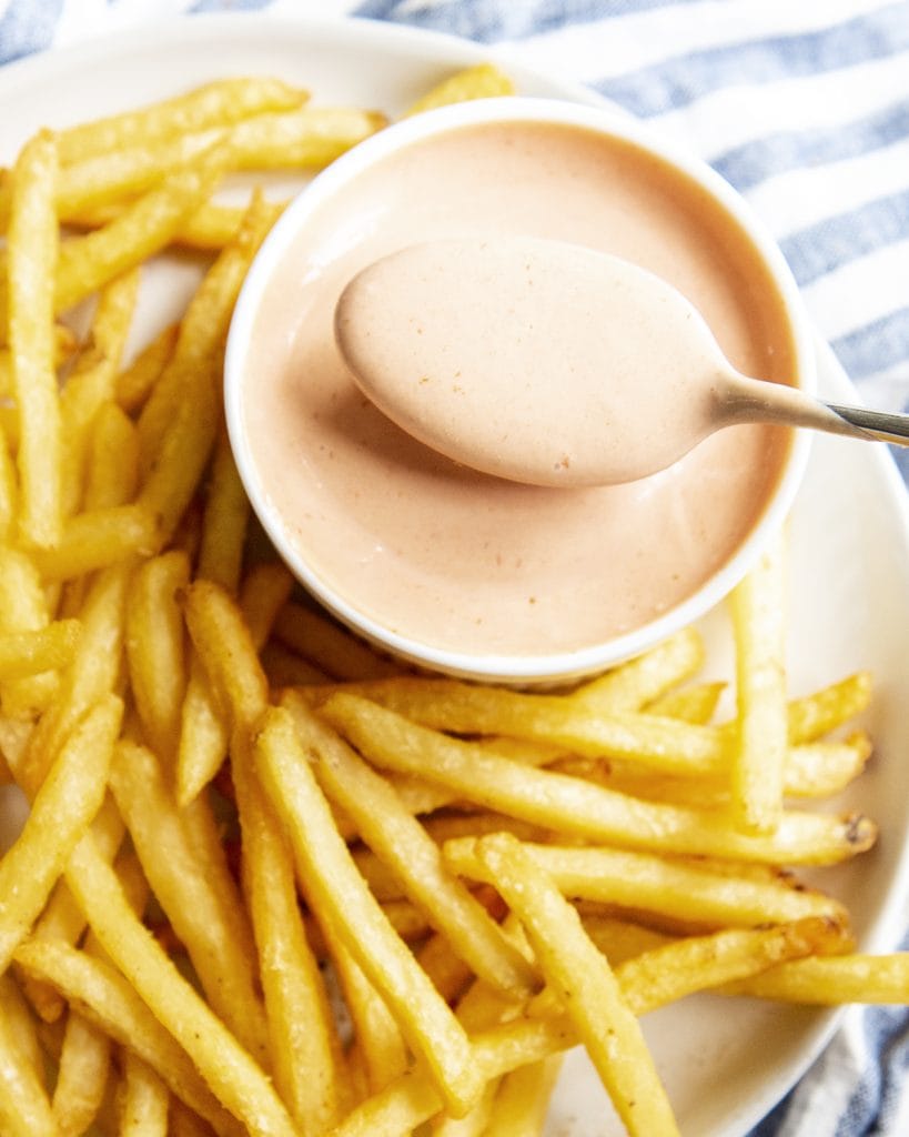 A spoonful of fry sauce being held above a bowl of fry sauce.
