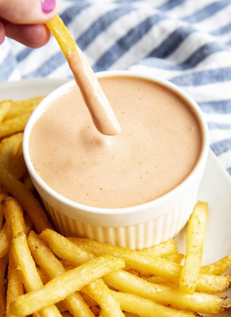 A french fry that was dipped into a bowl of fry sauce and is being lifted out.