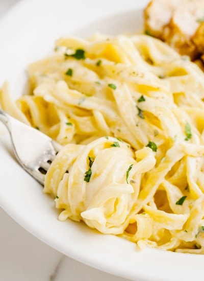 A plate of fettucine alfredo with noodles swirled around a fork on the plate.