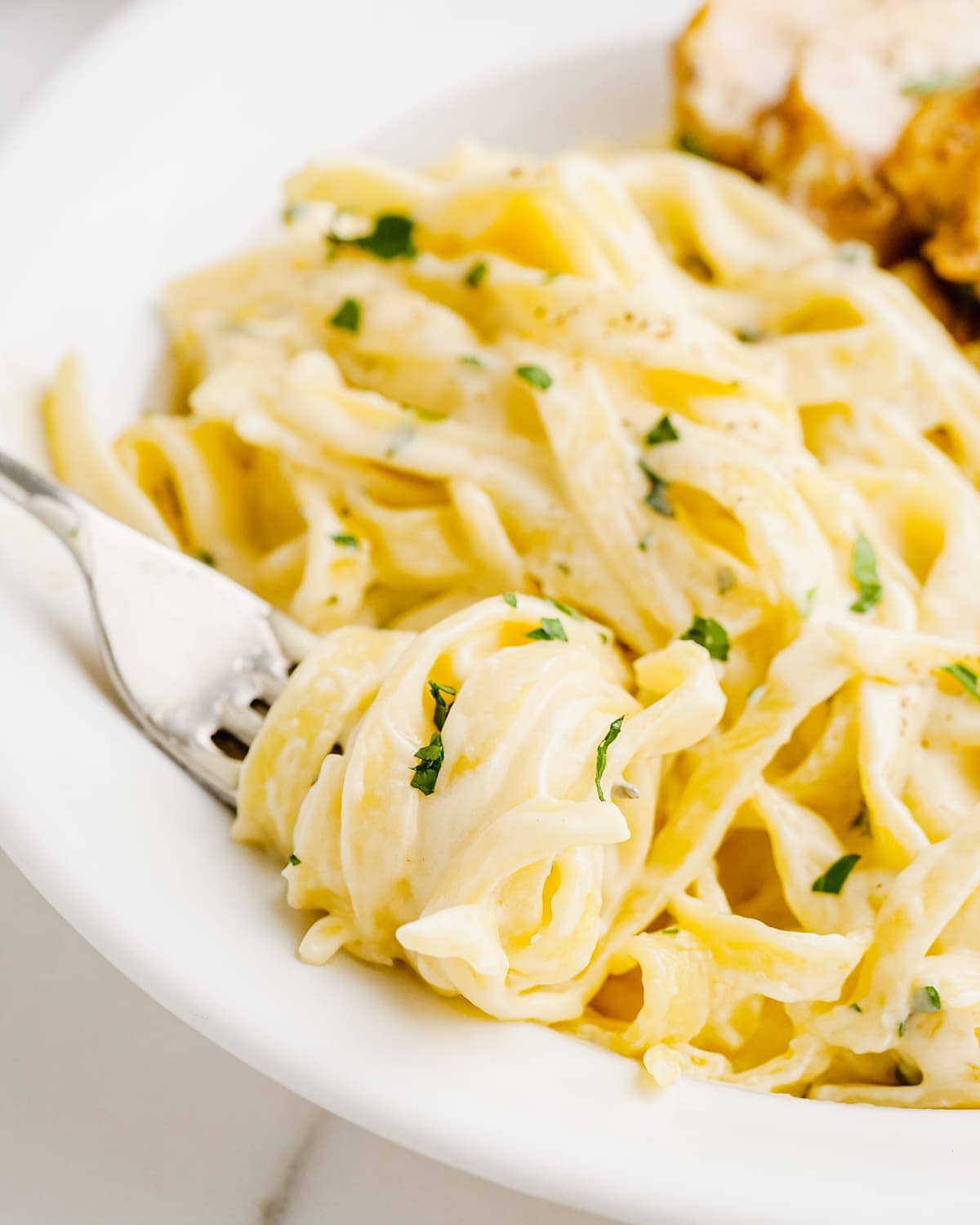 A plate of fettucine alfredo with noodles swirled around a fork on the plate.