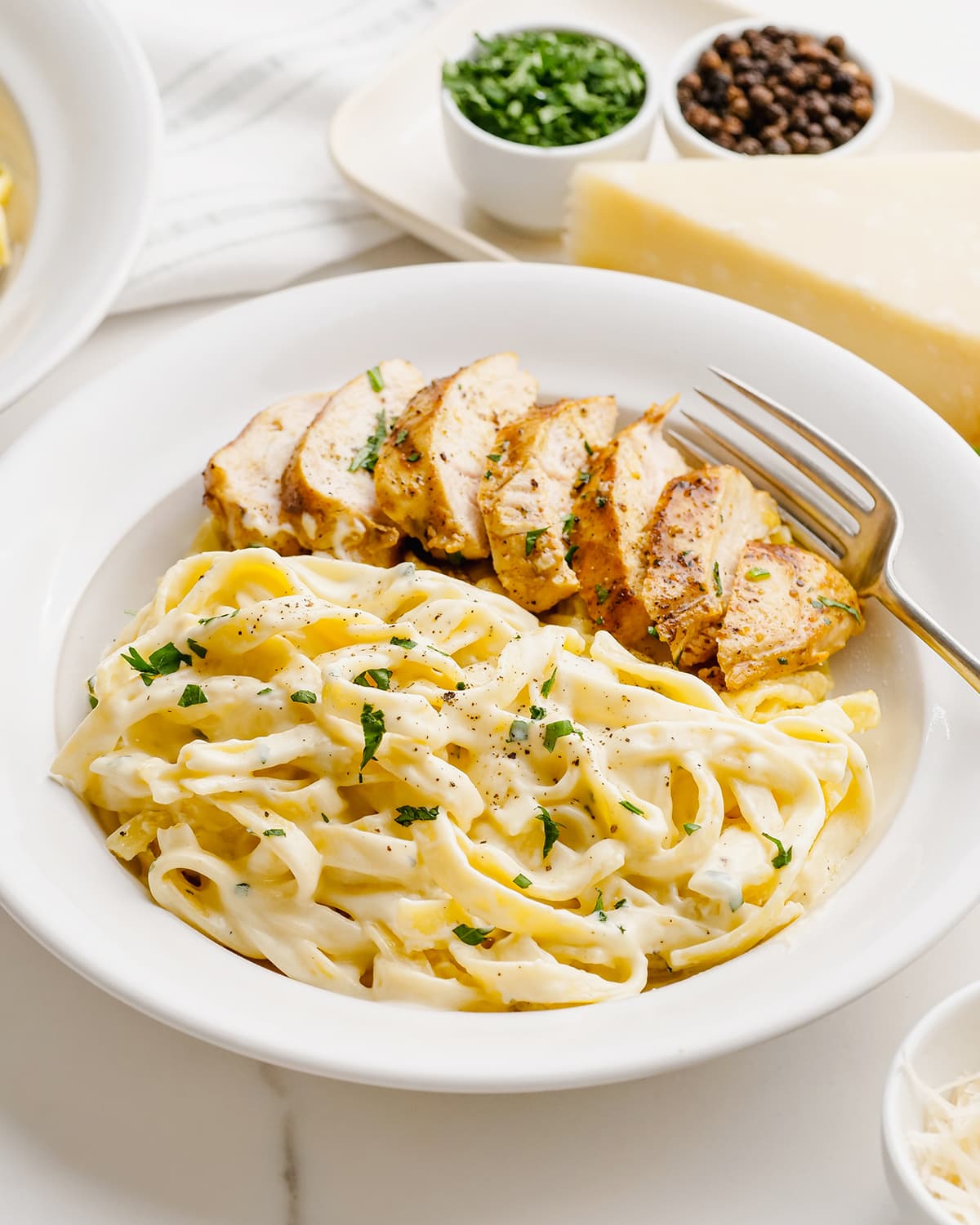 A plate of alfredo pasta with grilled chicken, all sprinkled with fresh parsley.