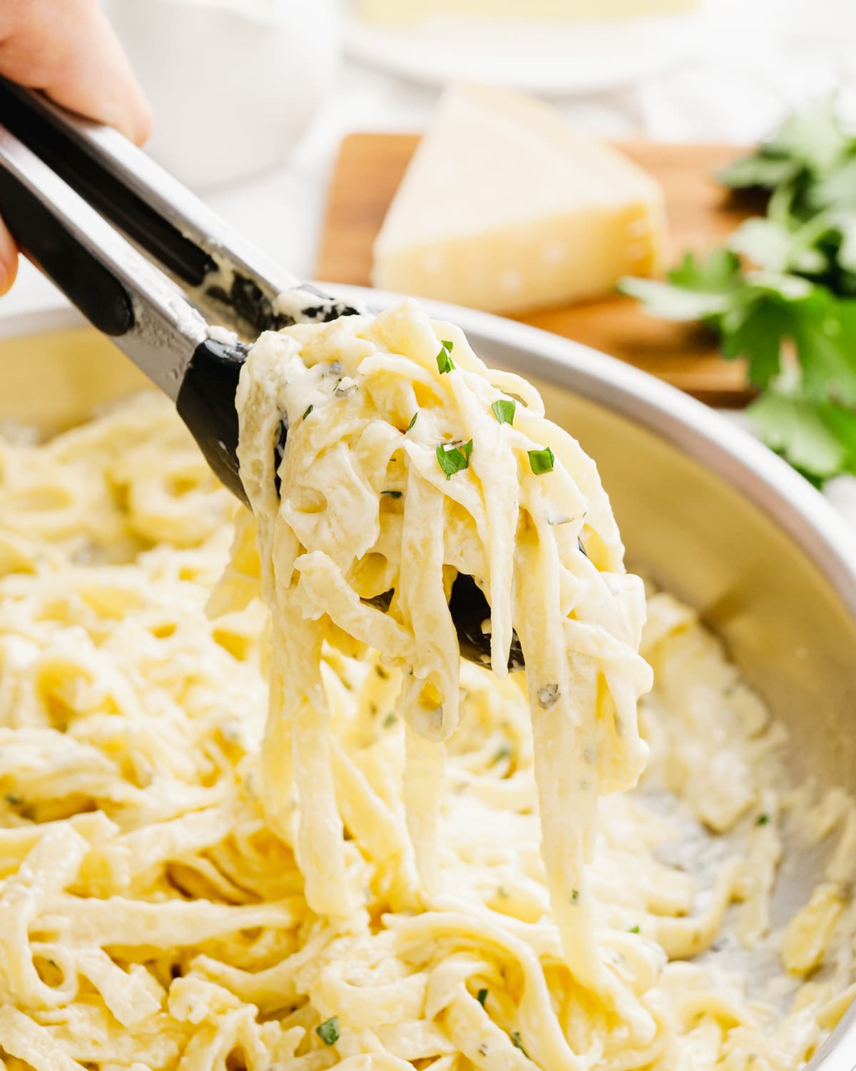 Alfredo sauce on fettucine noodles being held above a pot with tongs.