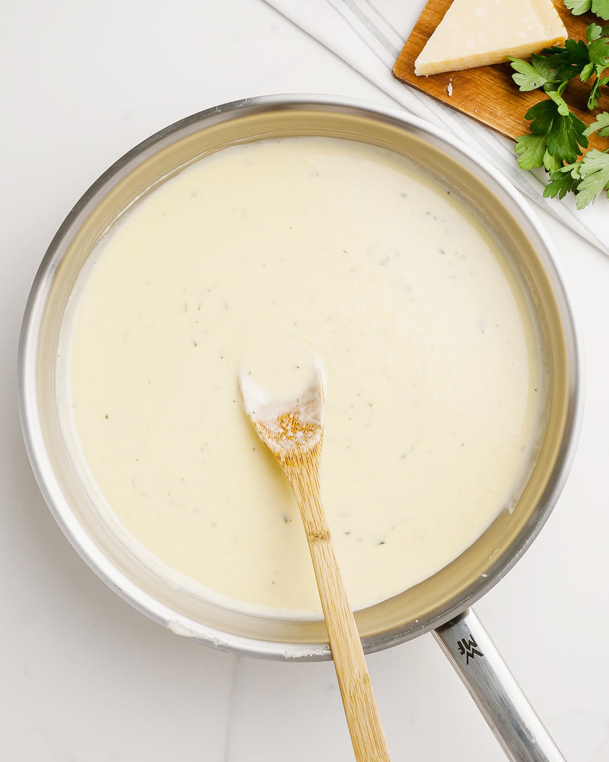 Alfredo sauce in a pan with a wooden spoon resting in the pan.