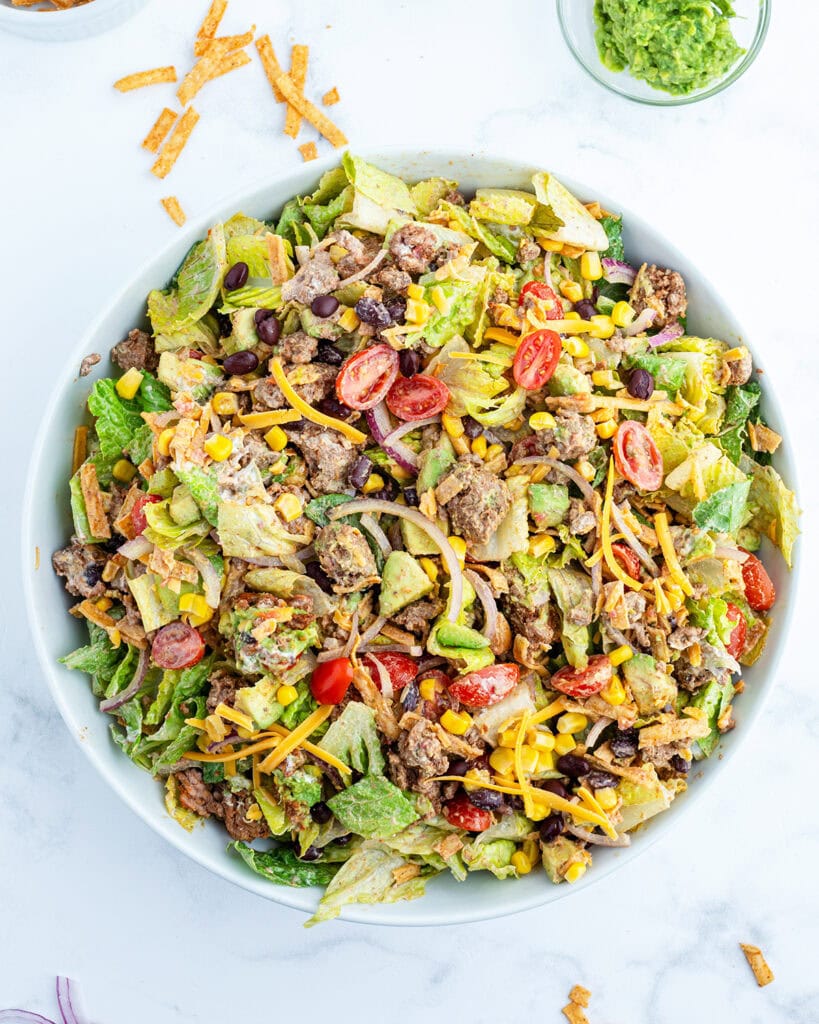 An overhead view of a large bowl of tossed taco salad with ground beef, lettuce, tomatoes, and cheese.