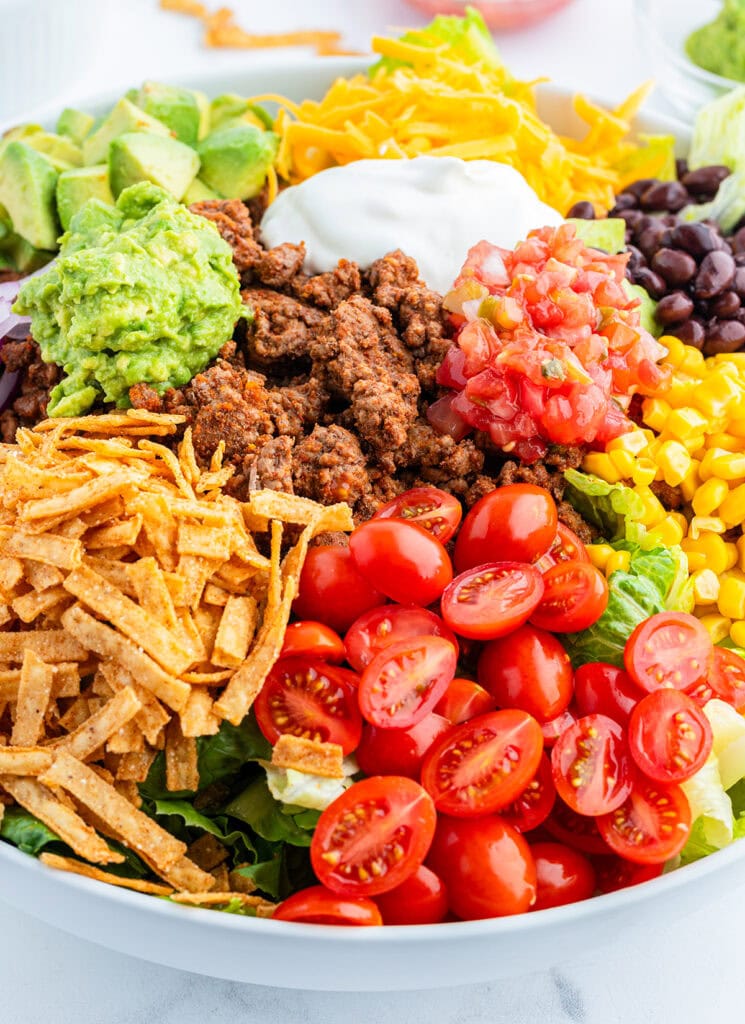 Beef taco salad toppings all in portions on top of a bowl of lettuce.