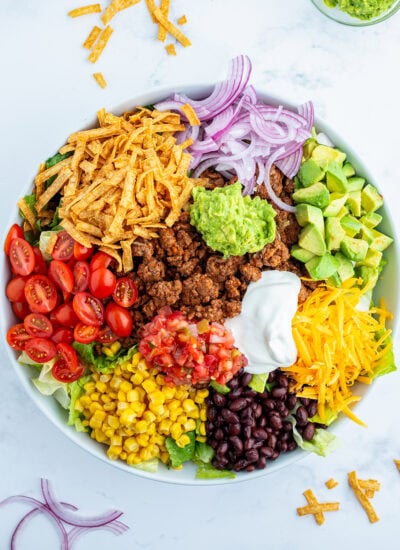 Beef taco salad toppings all in portions on top of a bowl of lettuce, like tomatoes, lettuce, red onion, avocado, cheese, and tortilla s trips.