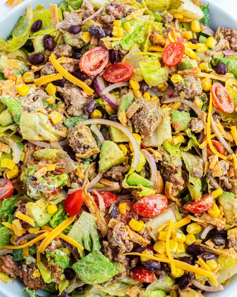 A close up view of a large bowl of tossed taco salad with ground beef, lettuce, tomatoes, and cheese.