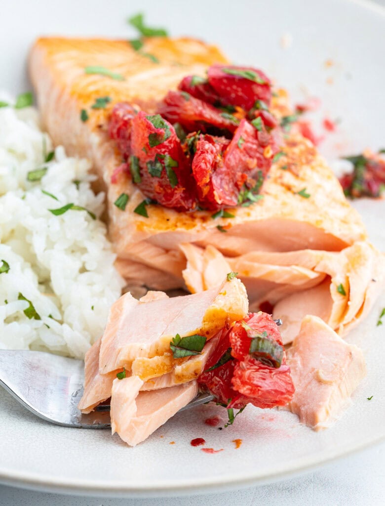 A flakey salmon fillet on a plate with a fork, flaking a piece of it off.