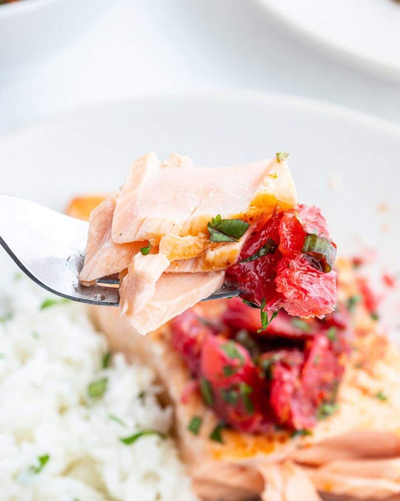 A forkful of salmon with a piece of red orange.