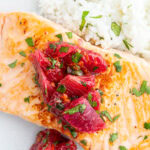 A plate of salmon, and rice topped with a citrus salsa.