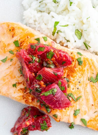 A plate of salmon, and rice topped with a citrus salsa.