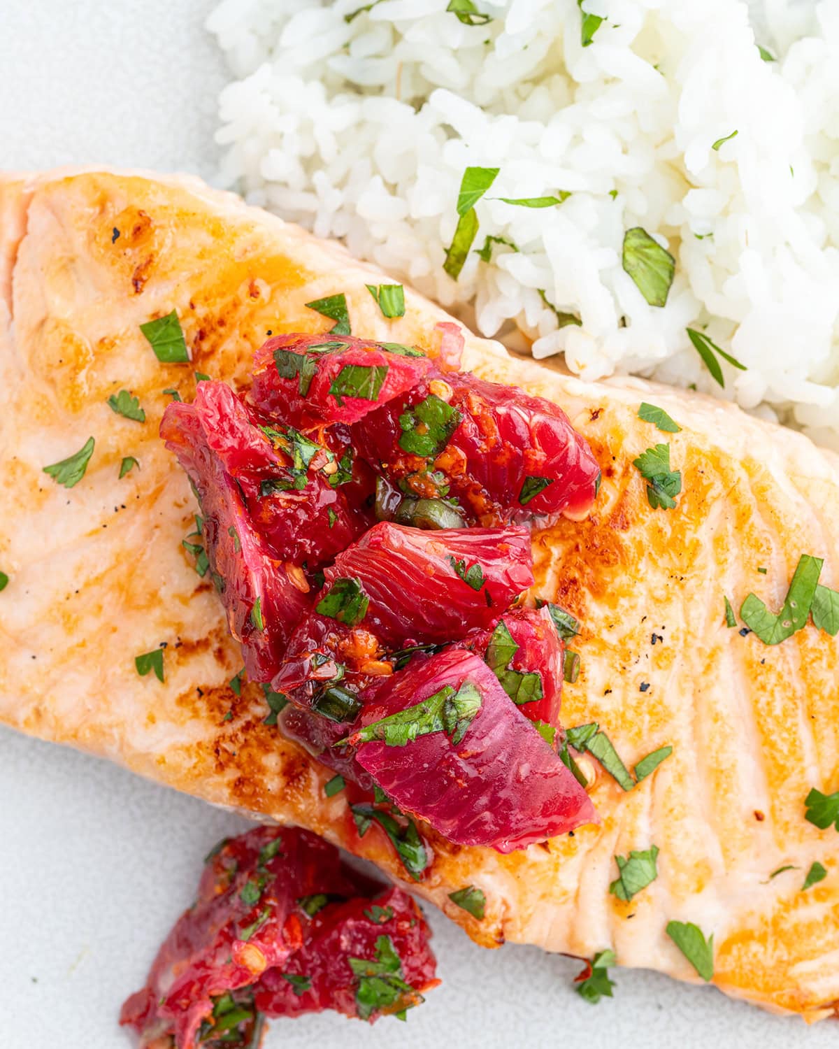 A plate of salmon, and rice topped with a citrus salsa.