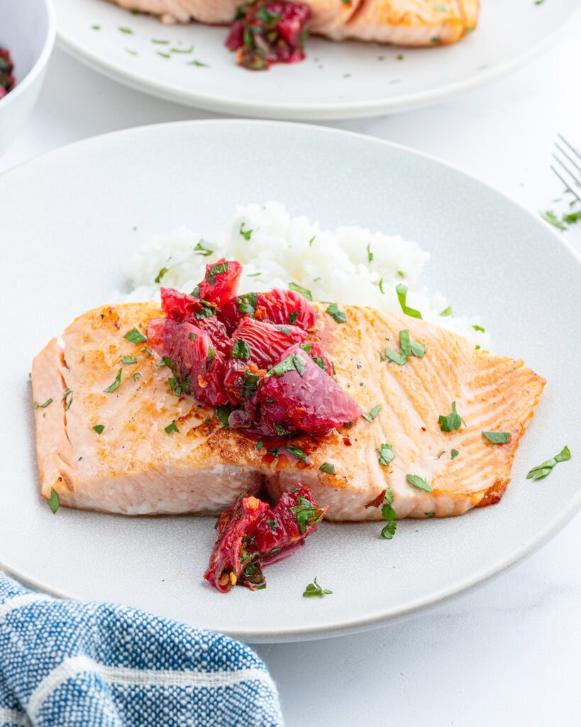 A plate of salmon, and rice topped with a citrus salsa.