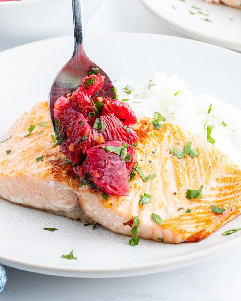 Blood orange salsa being set on a salmon fillet with a spoon.