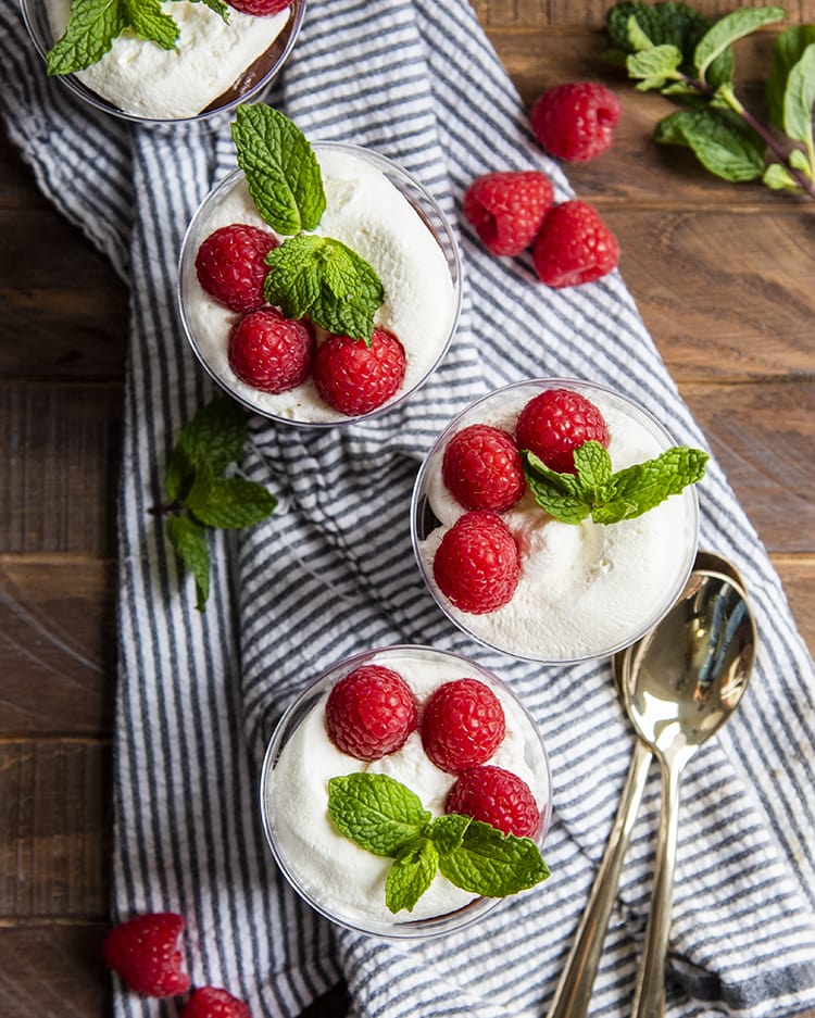 Cups of brownie trifles shot from above. You can see the white whipped cream, three raspberries, and a mint sprig on top.