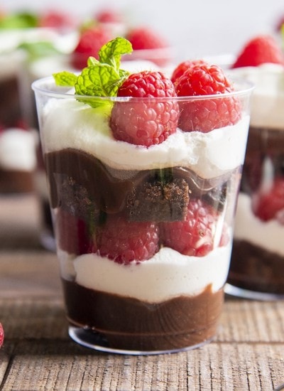 A brownie trifle cup with raspberries, whipped cream, brownie, and chocolate.