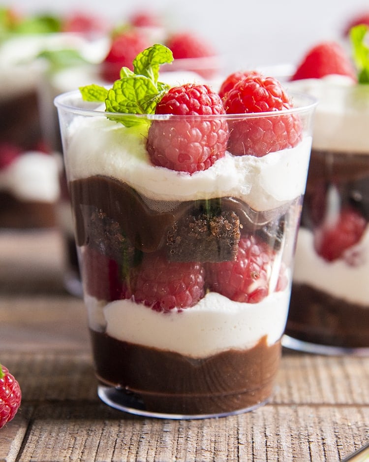 A brownie trifle cup with raspberries, whipped cream, brownie, and chocolate.