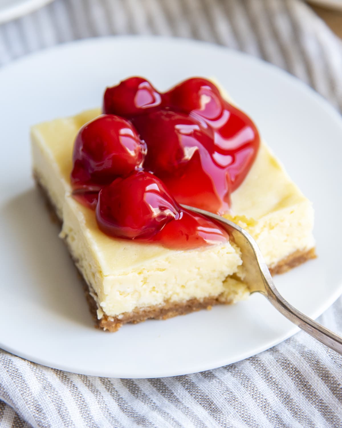 A cheesecake bar topped with cherry pie filling and a fork is cutting into it.